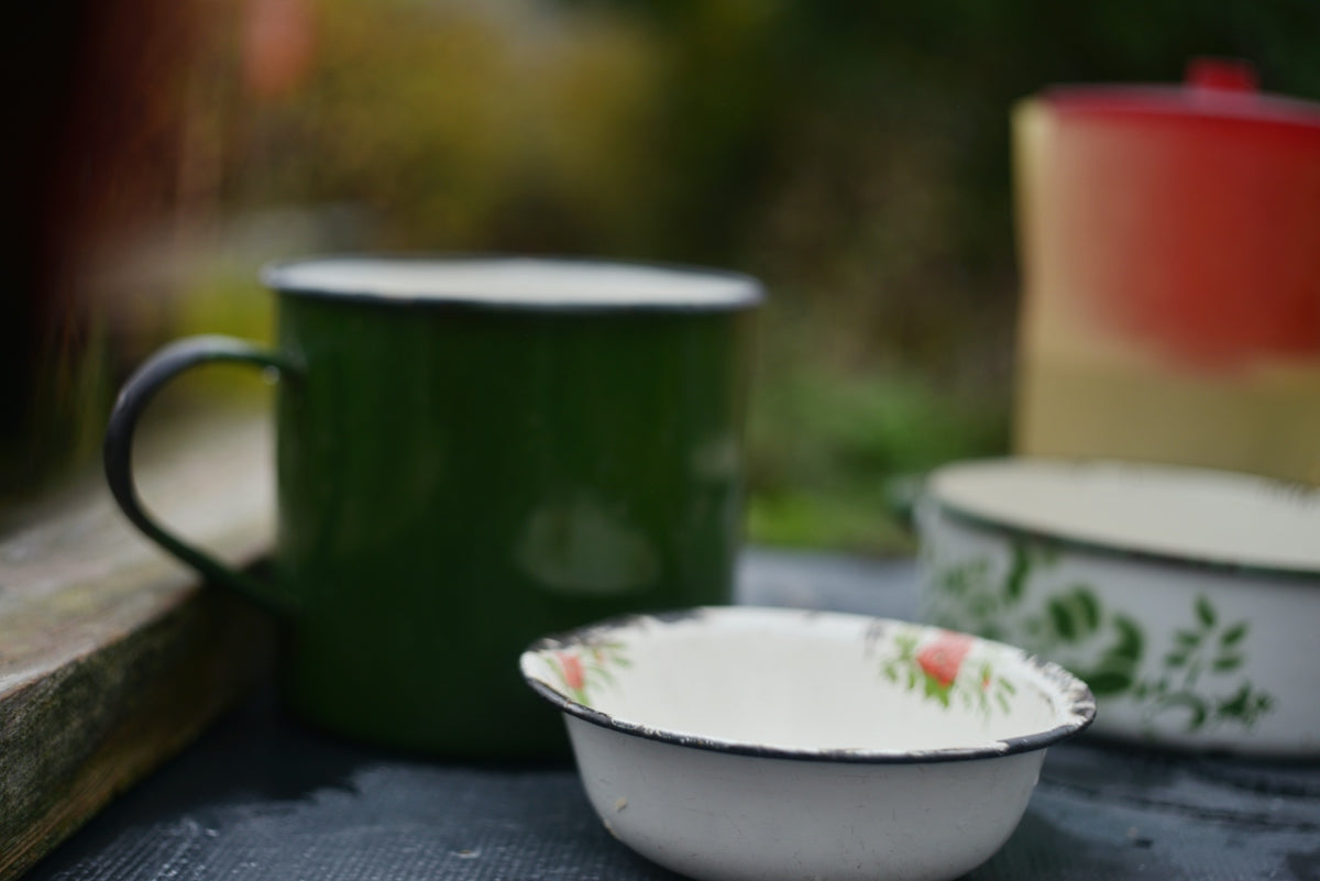 A green enamel mug beside a small white bowl with floral patterns on a dark surface